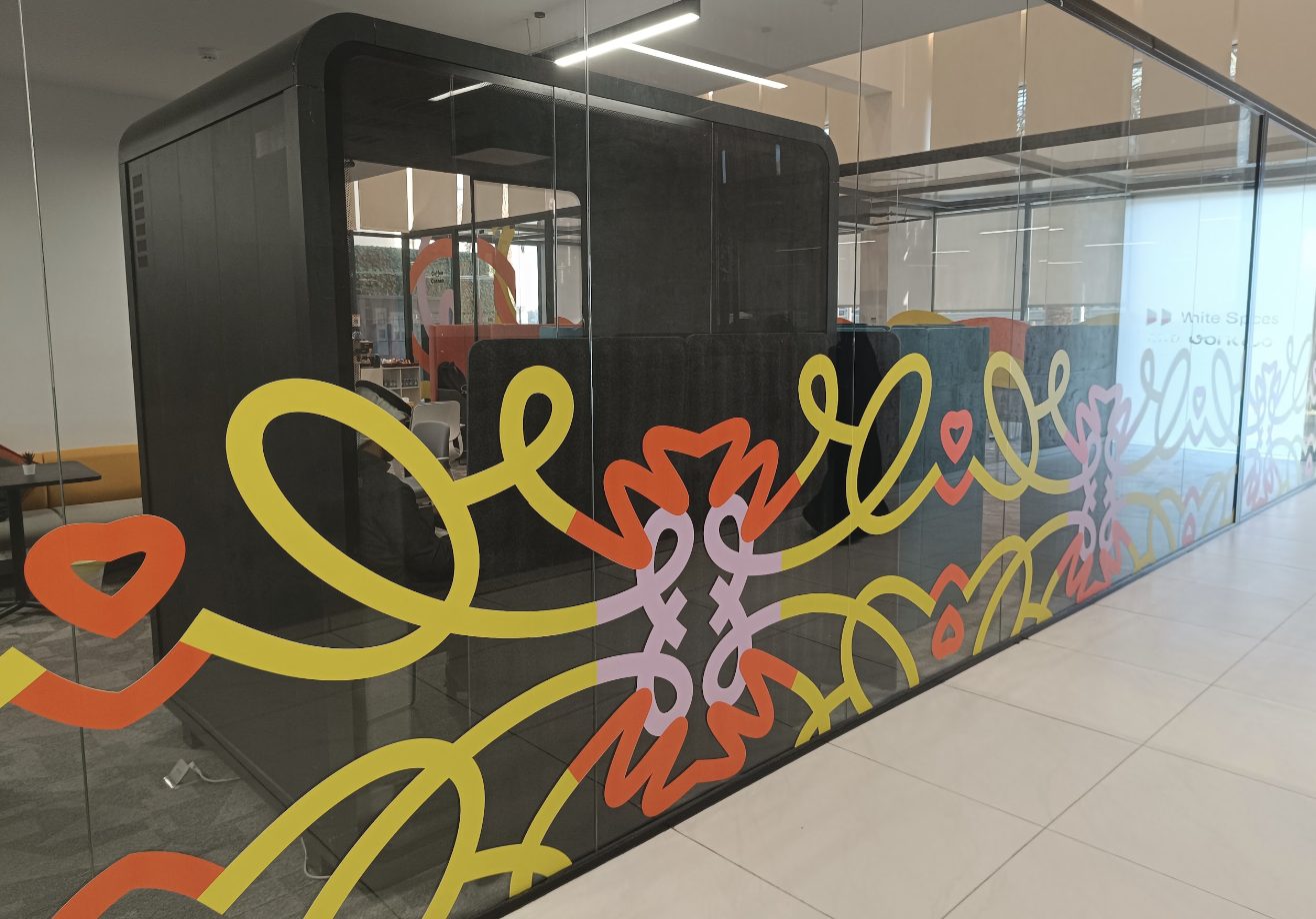 Glass phone booth with a bright squiggle mural at a White Spaces and Work&Co site in Jeddah